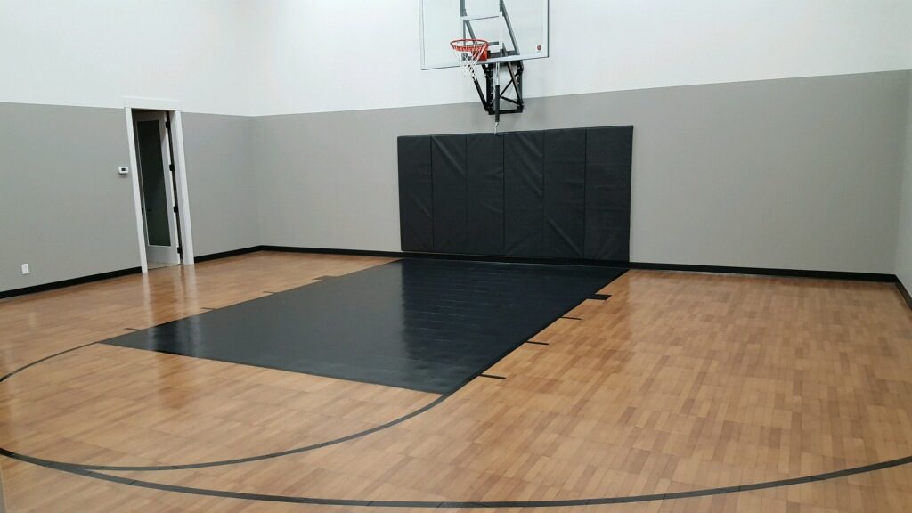 Millz House installed indoor basketball court in Eden Prairie featuring SnapSports Revolution Tuffshield athletic flooring in dark maple with black lane and black game lines and a 72 wall mount adjustable hoop