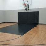 Millz House installed indoor basketball court in Eden Prairie featuring SnapSports Revolution Tuffshield athletic flooring in dark maple with black lane and black game lines and a 72 wall mount adjustable hoop