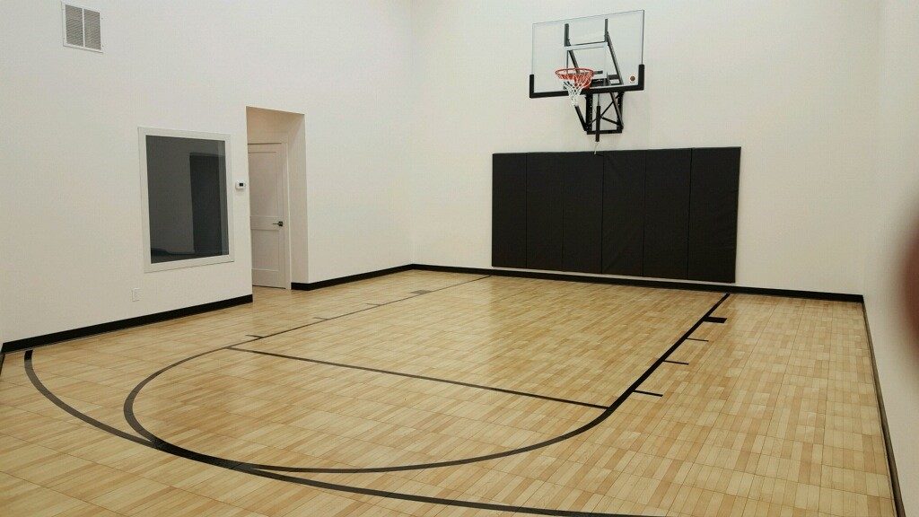 Indoor basketball court installed by Millz House using SnapSports athletic flooring in maple with wall mount hoop and black wall pads