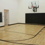 Indoor basketball court installed by Millz House using SnapSports athletic flooring in maple with wall mount hoop and black wall pads